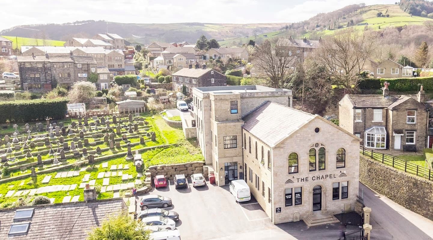 The Chapel from above: a restored stone chapel in Mytholmroyd with the green hills of the Calder Valley rising behind it.