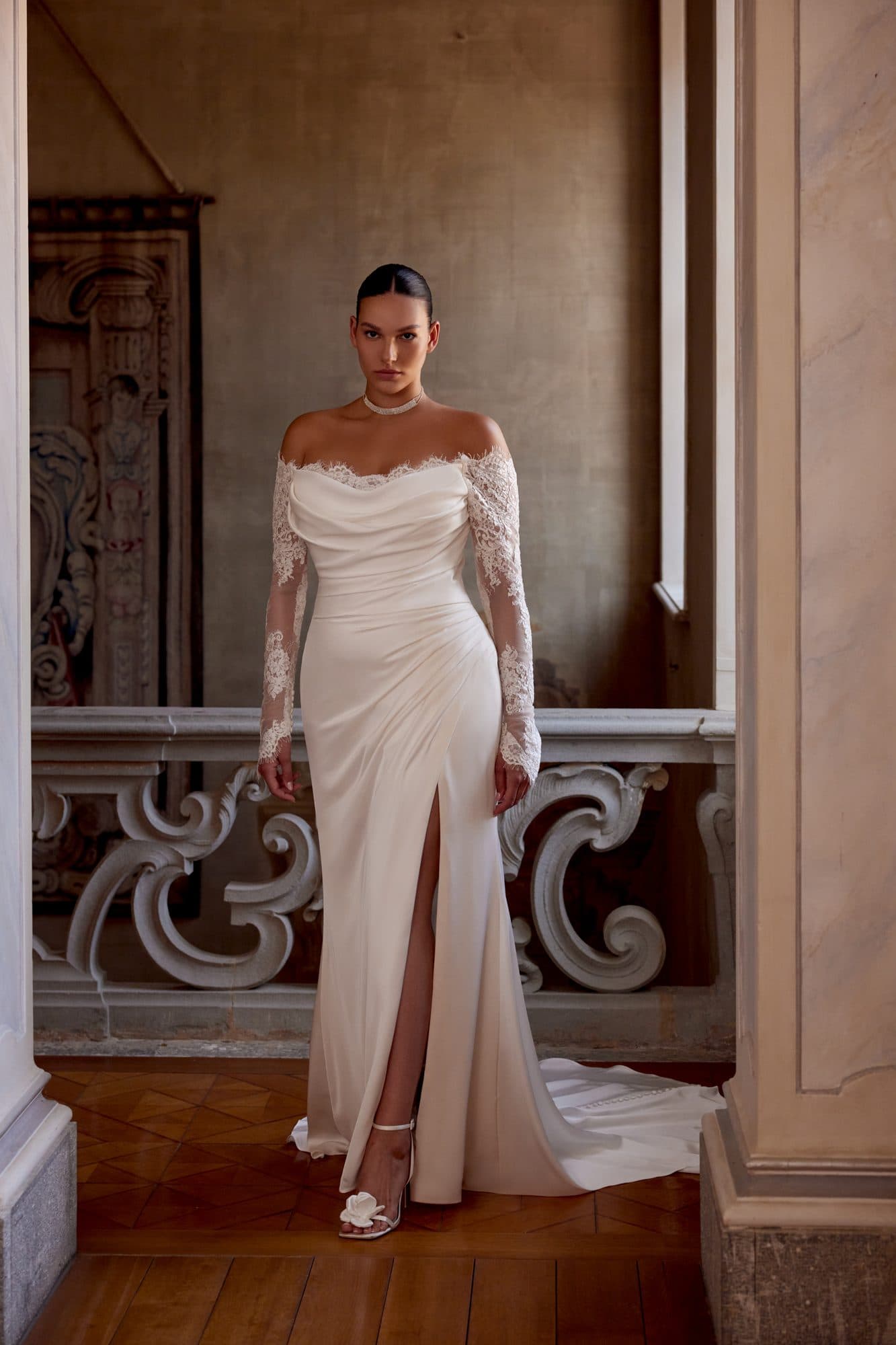 Front of the Justin Alexander Jessa gown, a fitted silhouette with off-the-shoulder lace sleeves and a leg slit.