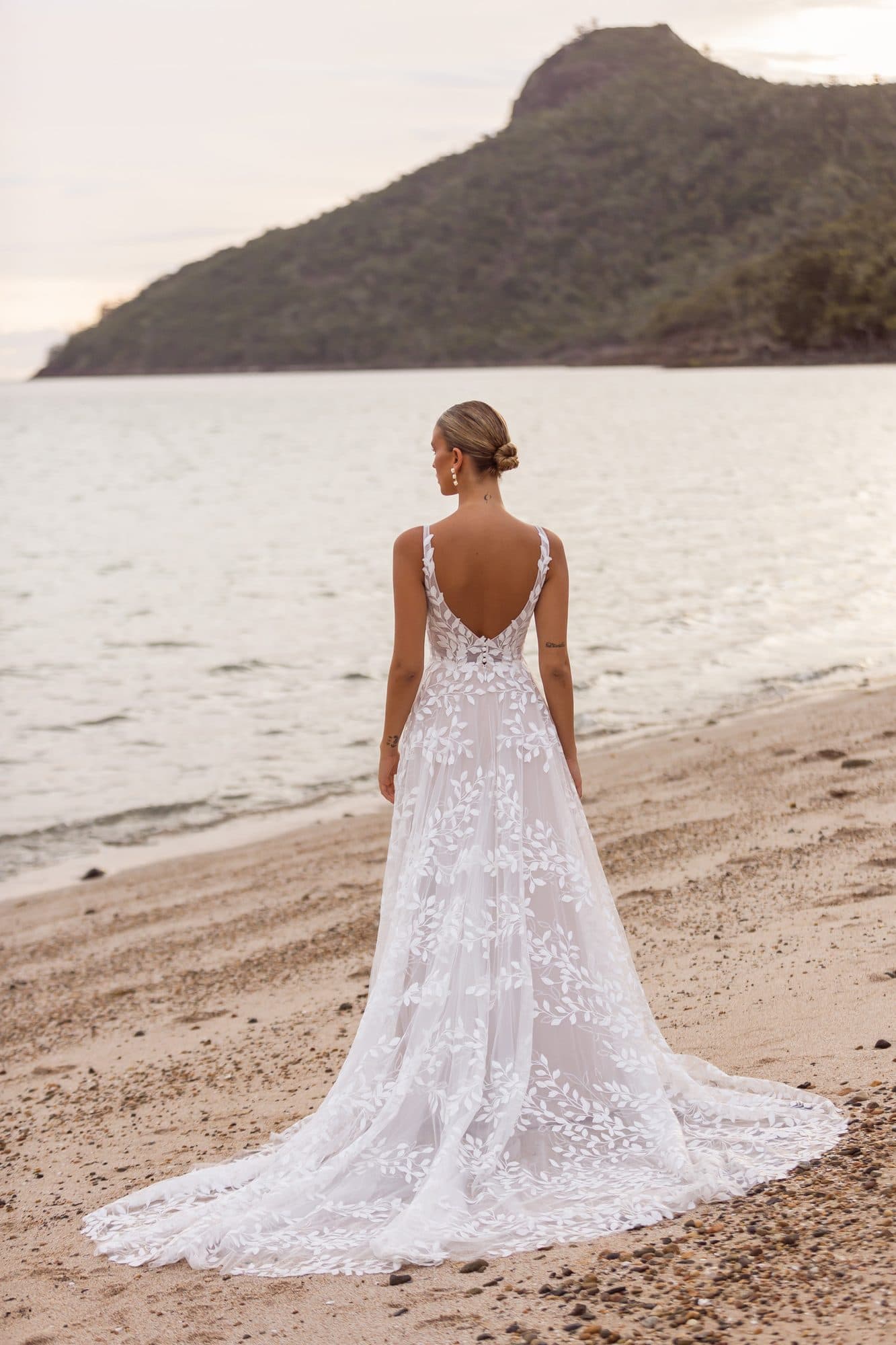 Back of the Madi Lane Jaya gown showing its V-back and sheer lace train on the sand.