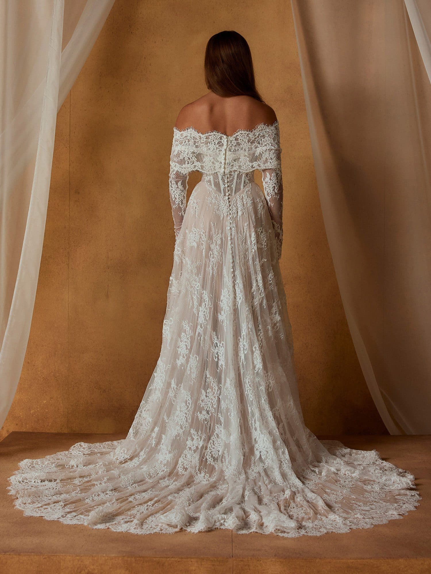 Back of the Madi Lane Nivaya gown showing its off-the-shoulder lace sleeves and scalloped train.