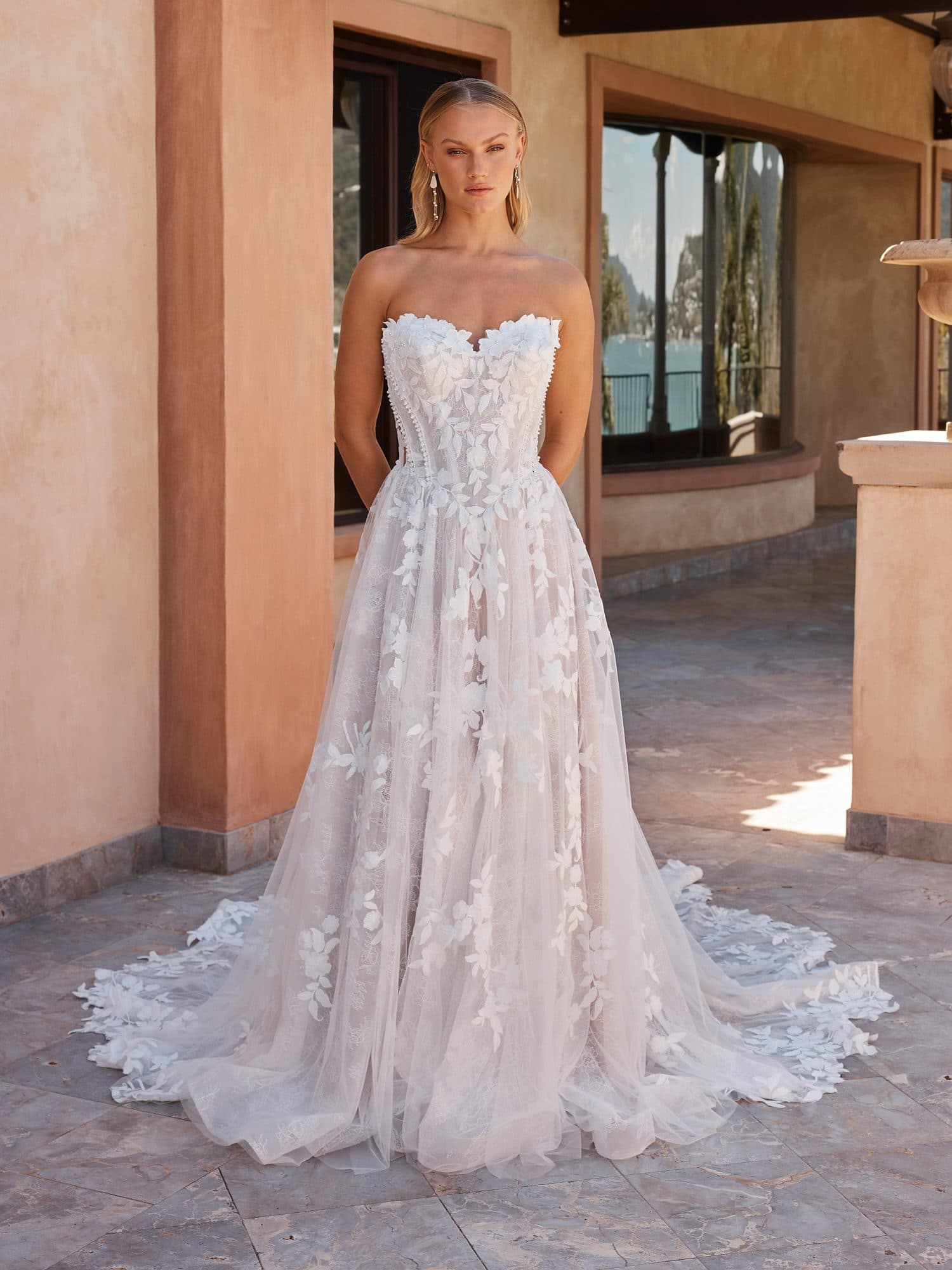 Front of the Madi Lane Osha gown, a sweetheart A-line in three-dimensional floral lace, in a sunlit courtyard.