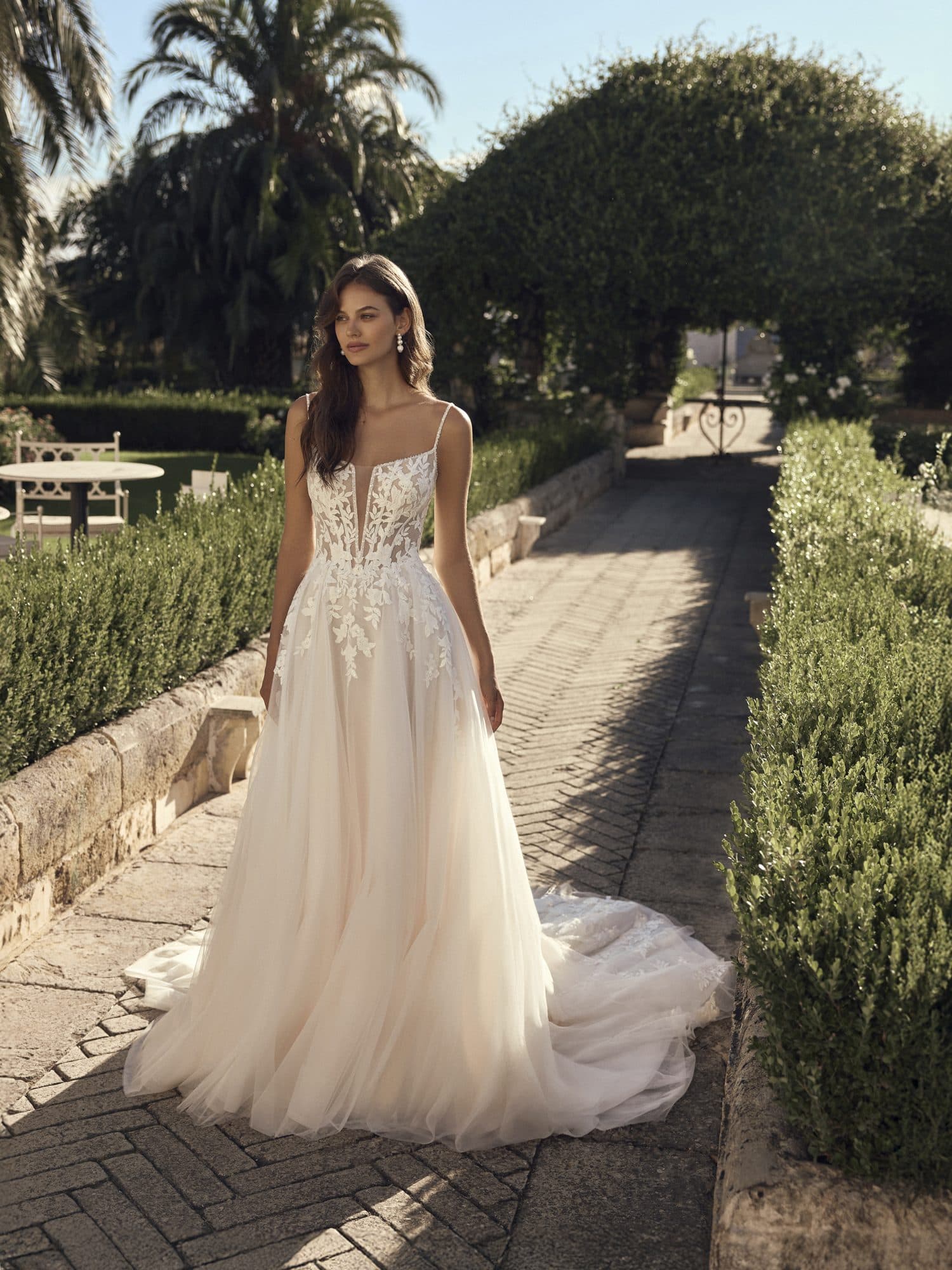 Front of the Modeca Moyra gown, a tulle A-line with a plunging lace bodice, in a formal garden.