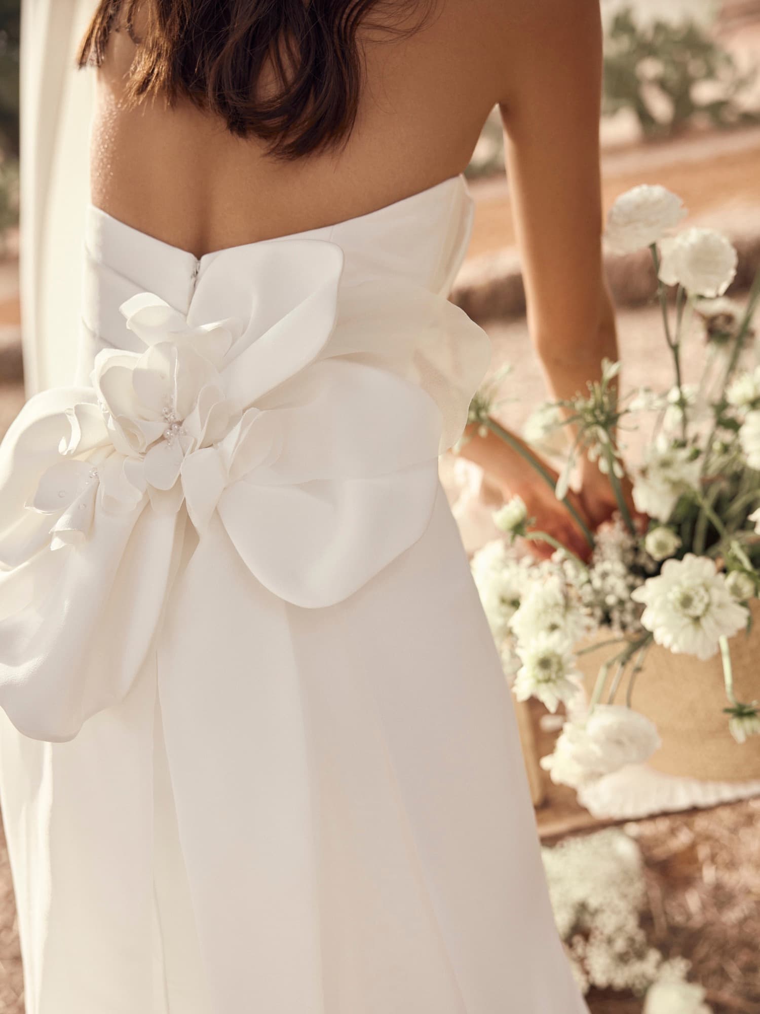 Close detail of a Modeca gown with a sculpted organza bow at the back, the bride holding a bouquet of white flowers.